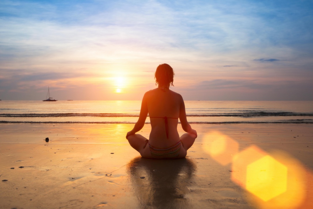 Person meditating on beach at sunset